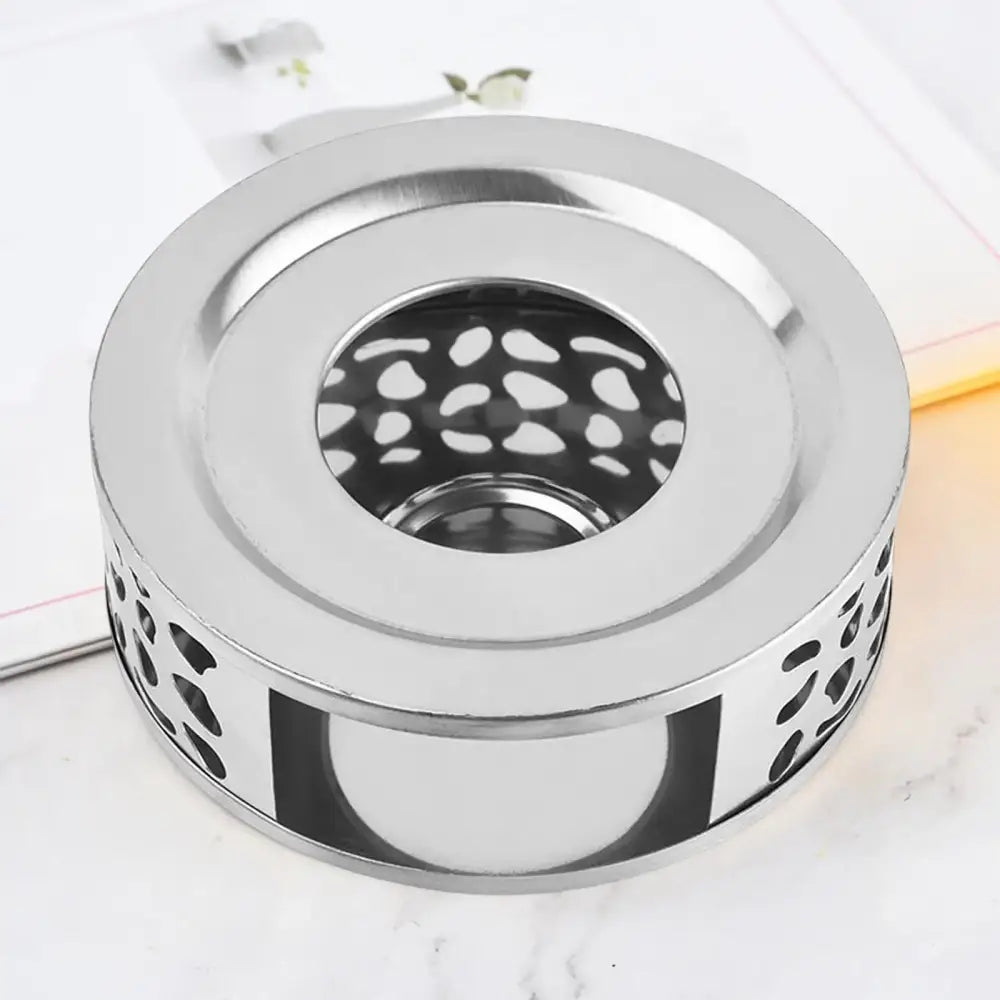 Silver finish stainless steel teapot warmer with candle glow, tea ritual table scene