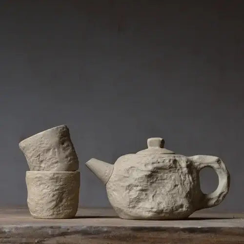 Stone teapot next to two matching cups, earthy olive-grey color