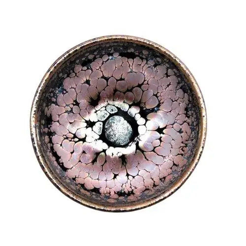 Handcrafted Tenmoku chawan with dark iron glaze on wooden table, side view