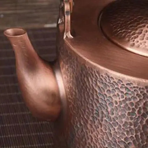 Copper tea kettle spout pouring hot water into a teapot