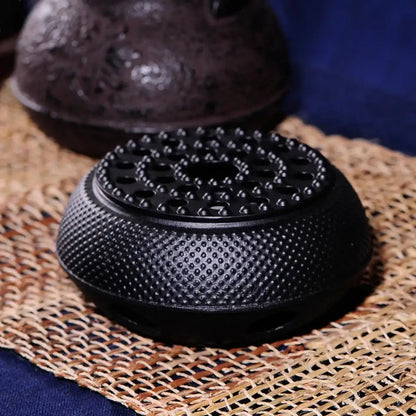 Black cast iron teapot warmer on a wooden table, matte finish detail