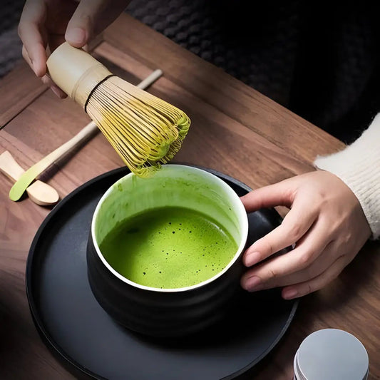 Hands holding black ceramic matcha bowl with green matcha tea