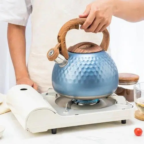 Blue enamel whistling kettle on gas stove with steam rising from spout