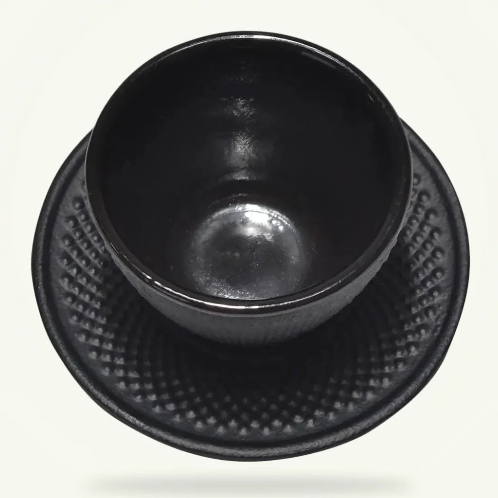 Black cast iron tea cup and saucer set with enamel interior on plain background