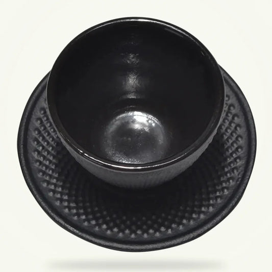 Black cast iron tea cup and saucer set with enamel interior on plain background