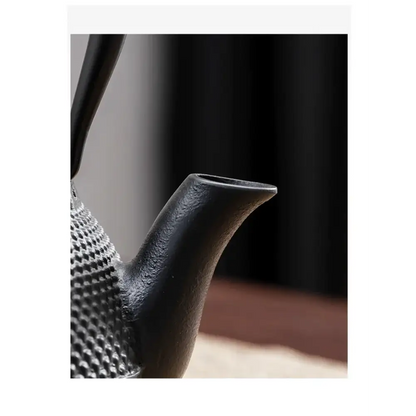 Cast iron teapot beside a cup of brewed tea and loose tea leaves
