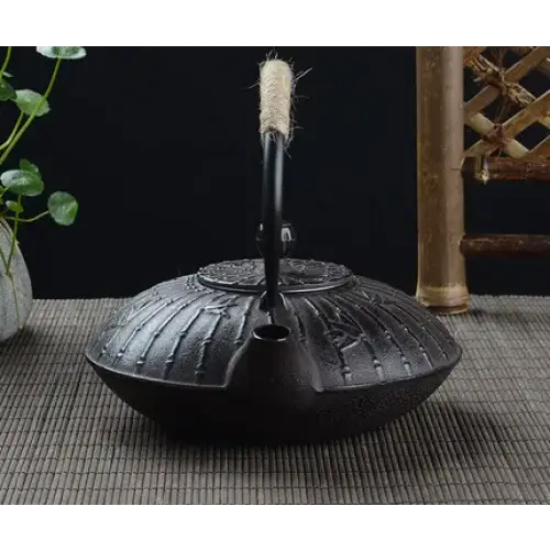 Cast iron teapot bamboo design pouring loose leaf tea into ceramic cup