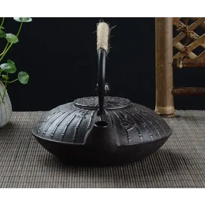 Cast iron teapot bamboo design pouring loose leaf tea into ceramic cup