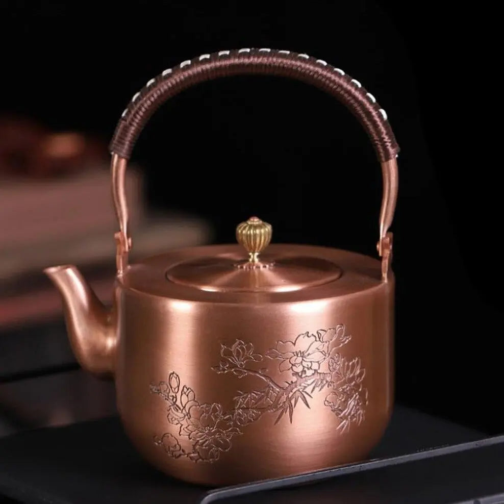 Chinese copper teapot with engraved flower motif, angled view showing handle and spout
