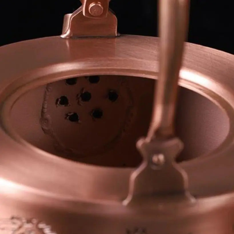 Copper teapot with engraved floral pattern, side detail showing motif depth and warm patina