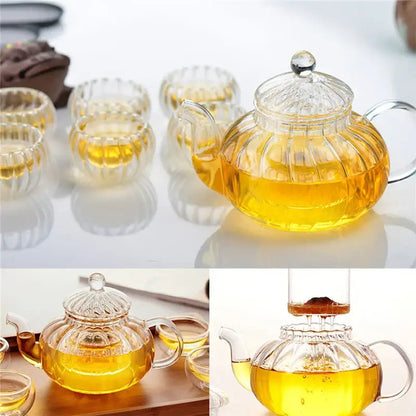 Glass teapot resting on candle warmer base with six cups arranged around it