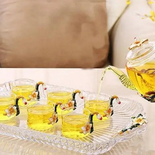 Floral glass teapot with all six cups arranged on wooden surface