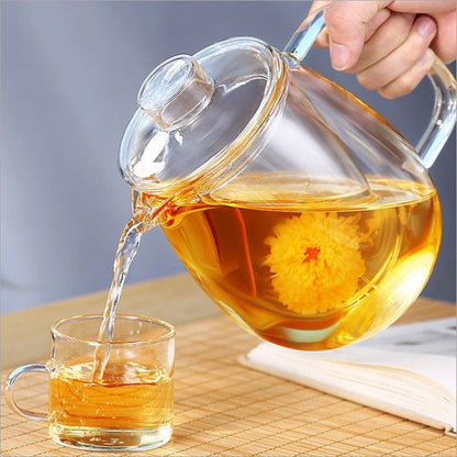 Glass flowering tea teapot pouring green tea into cup from above