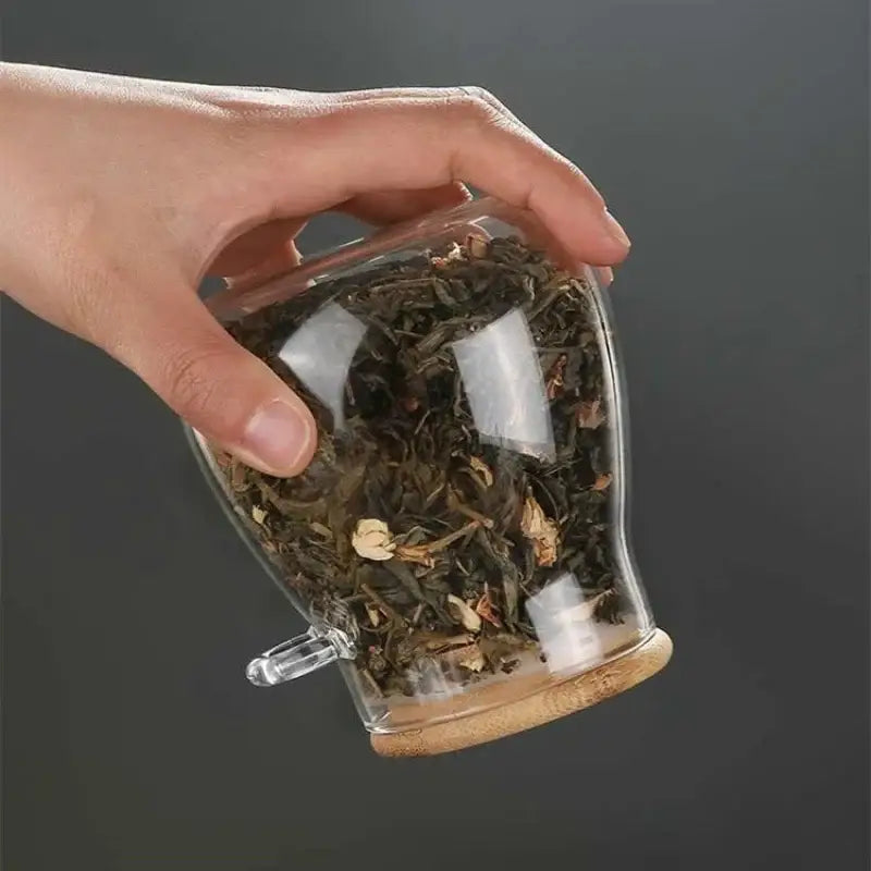 Glass teapot with bamboo lid and wooden spoon on natural surface, loose-leaf tea accessories