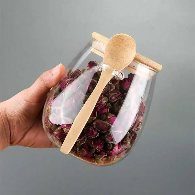 Glass teapot with bamboo lid pouring loose-leaf tea into a cup, clear borosilicate body