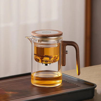 Pouring brewed loose leaf tea from glass teapot with wooden handle into ceramic cup