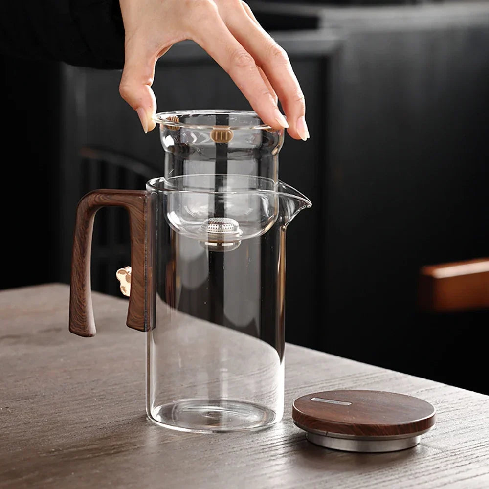 Pouring brewed loose-leaf tea from glass teapot with wood handle into a cup