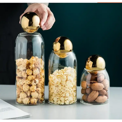 Airtight glass tea storage canister with golden lid sitting on a kitchen shelf