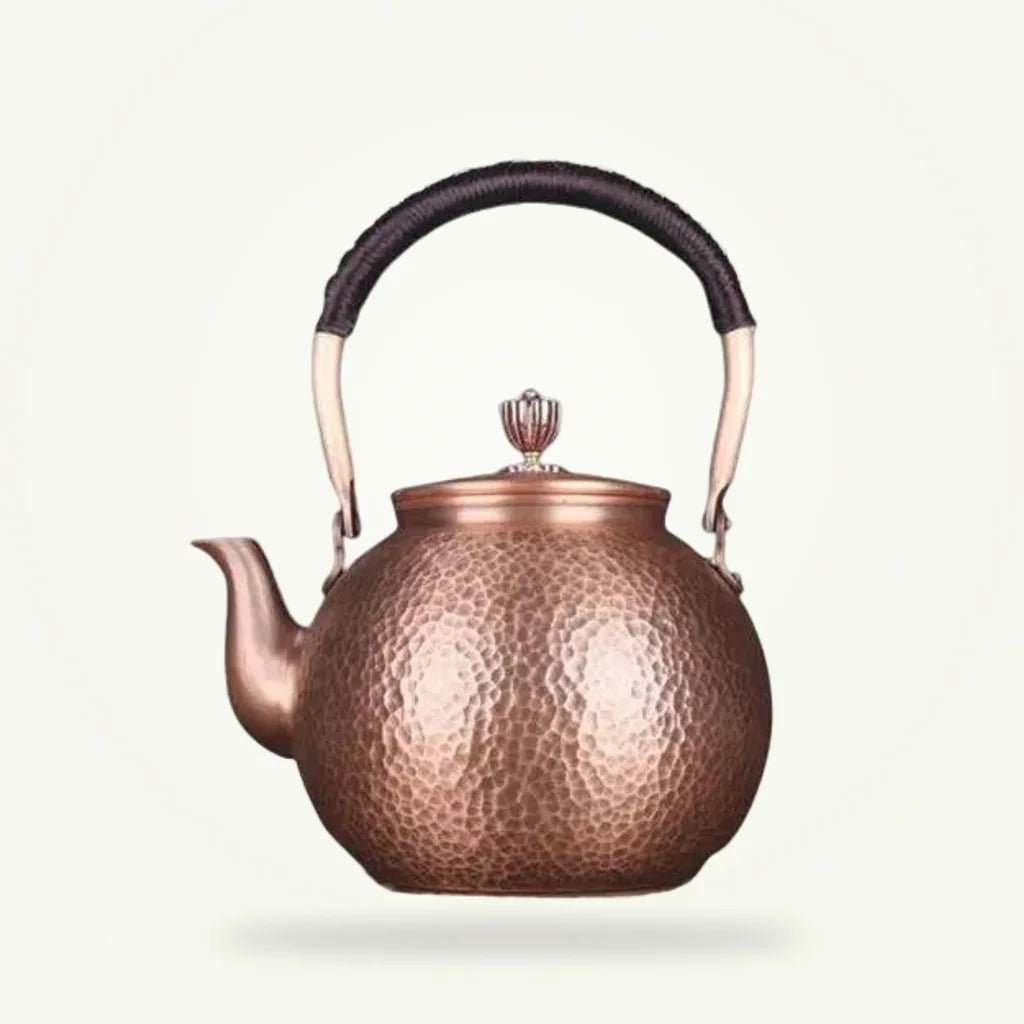 Hand-forged copper tea kettle 1300 ml on plain background, hammered surface detail