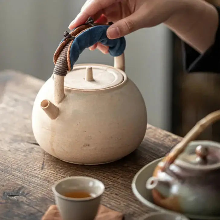 Teapot handle cover in blue on a teapot with tea cup