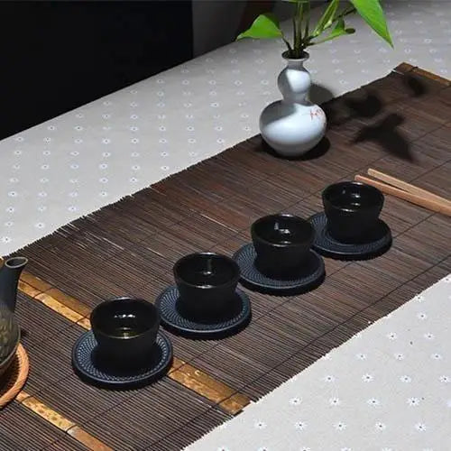 Black cast iron teacup and matching saucer on a wooden table surface
