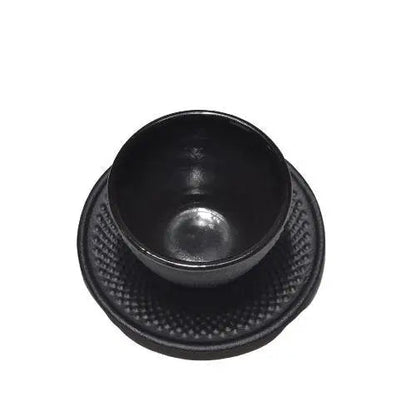 Black cast iron teacup with saucer viewed from above on dark table