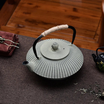 Cast iron tetsubin teapot pouring loose-leaf tea into ceramic cup, warm kitchen light