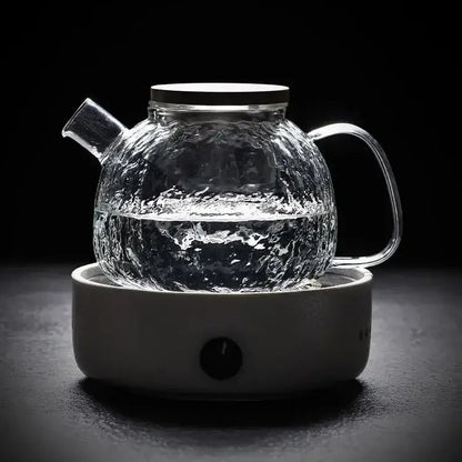 Glass teapot pouring brewed tea into a white ceramic cup