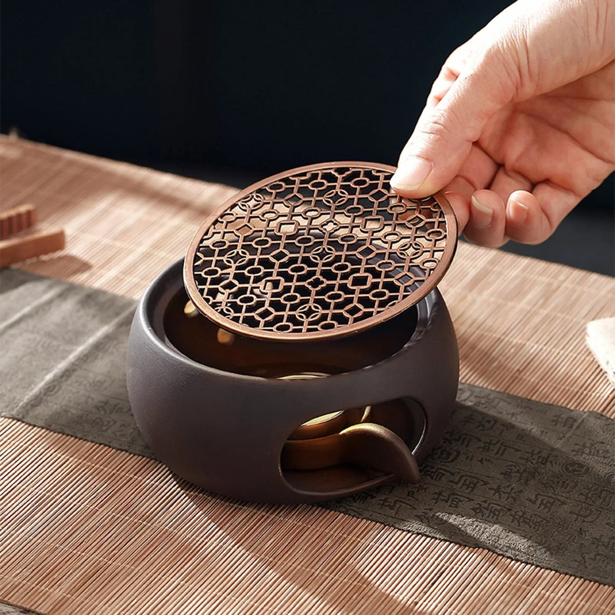 Candle tea warmer with sculpted grid resting on wooden table beside teacup