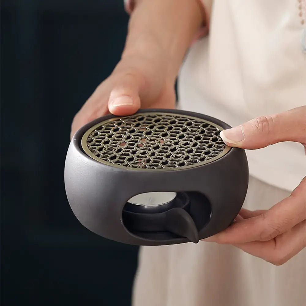 Japanese tea warmer with sculpted grid and lit tea light candle glowing underneath