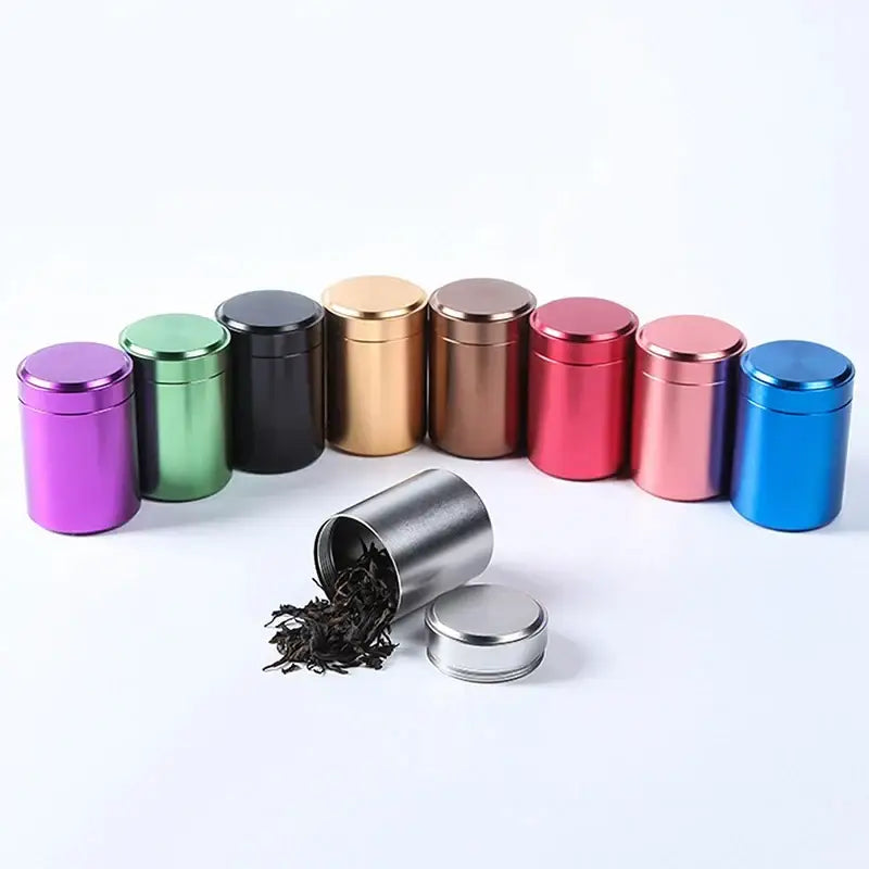 Stainless steel tea tin canister next to fresh loose leaf tea leaves on a wooden surface