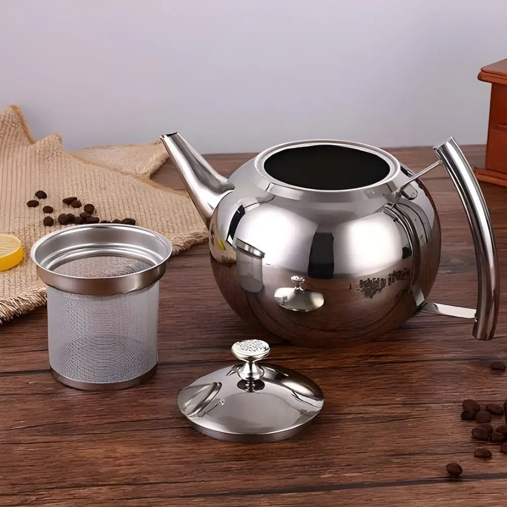 Stainless steel teapot styled on wooden tray with tea cups and loose leaves