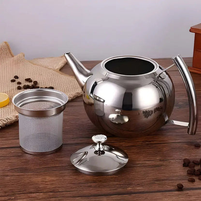 Stainless steel teapot styled on wooden tray with tea cups and loose leaves