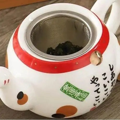 Close-up of lucky cat painted motif on white porcelain teapot