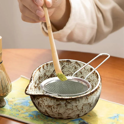 Whisking matcha powder in ceramic bowl with bamboo chasen, foam forming at surface