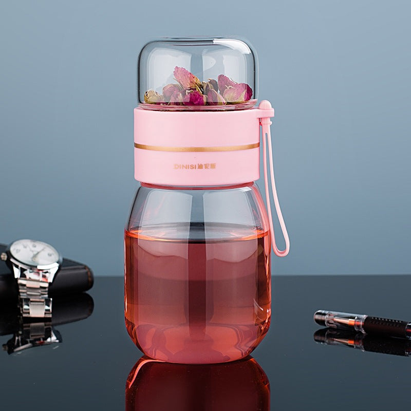 Portable glass teapot with infuser on wooden desk next to tea tin