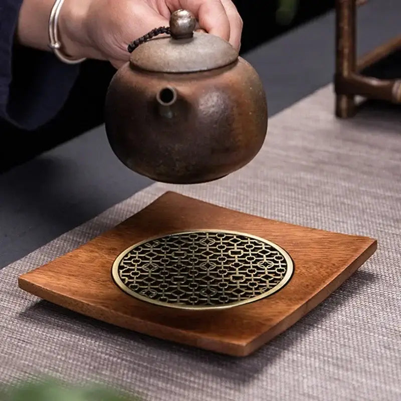 Natural wood teapot trivet with grid pattern resting on a wooden table