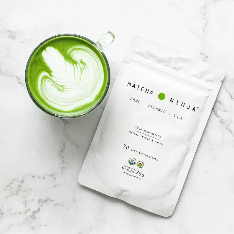 Organic matcha green tea powder in a bowl with a bamboo whisk