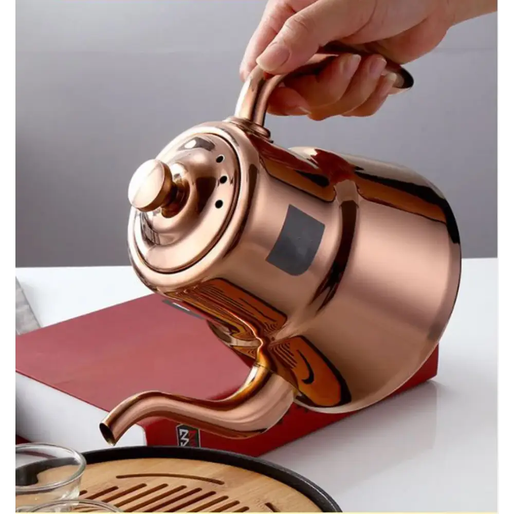 Polished stainless steel teapot pouring brewed loose-leaf tea into a white cup