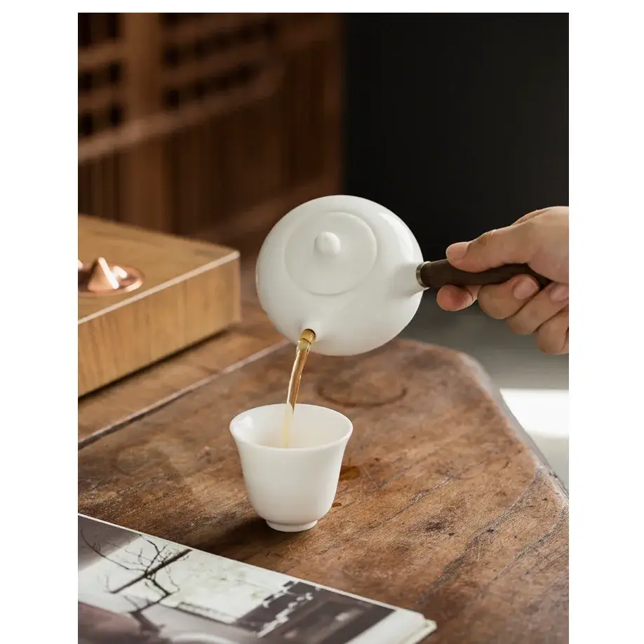 Porcelain teapot with infuser, pouring tea into a cup