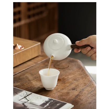 Porcelain teapot with infuser, pouring tea into a cup