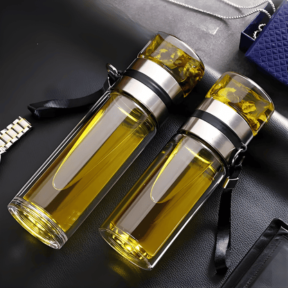 Portable glass tea bottle with stainless steel infuser on an office desk, commuter context