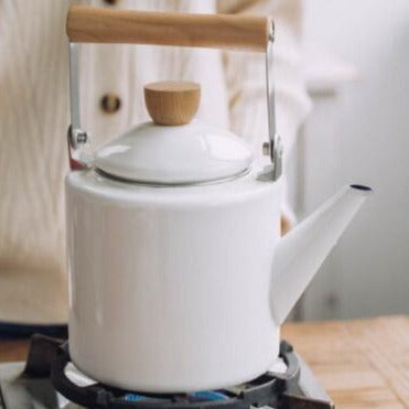 Scandinavian teapot on wooden board surrounded by loose tea leaves