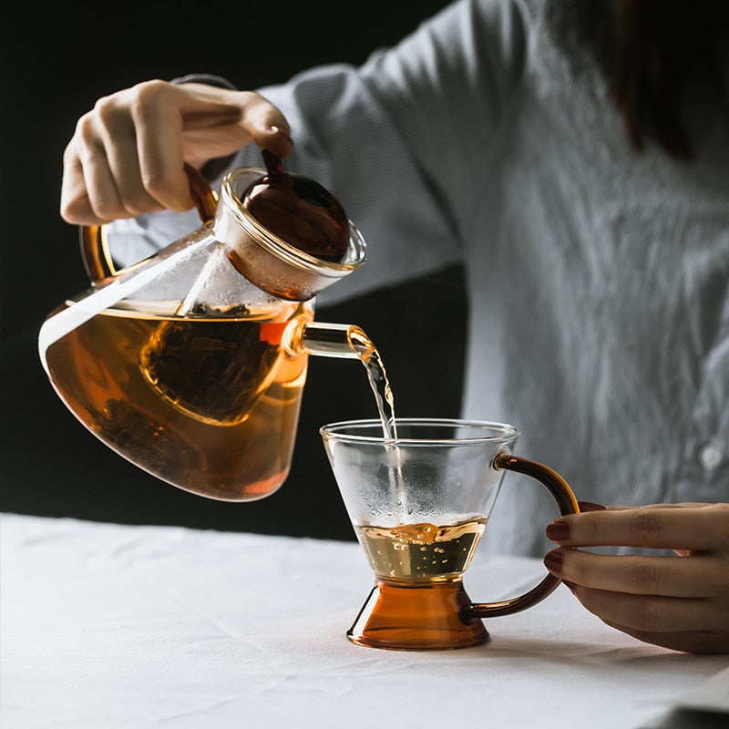 Scandinavian glass teapot with orange accent cup on wooden surface