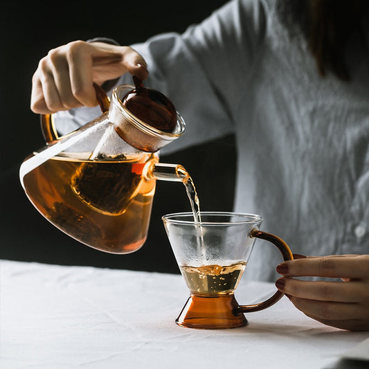 Scandinavian glass teapot with orange accent cup on wooden surface