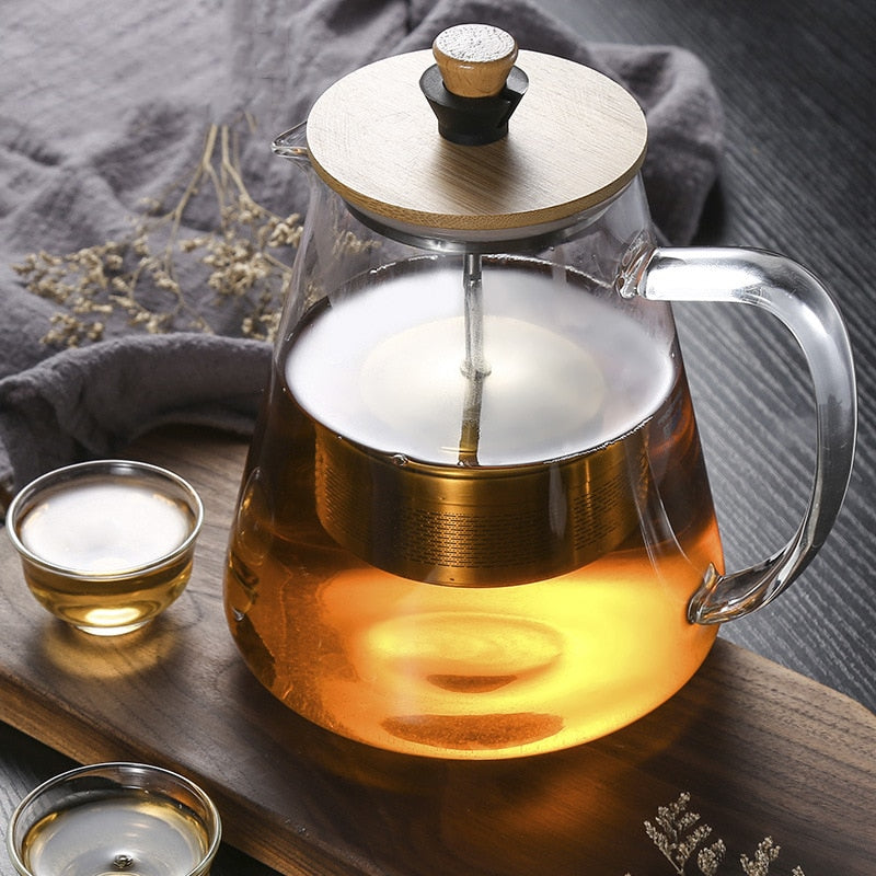 Glass teapot with infuser resting on a wooden table, warm light