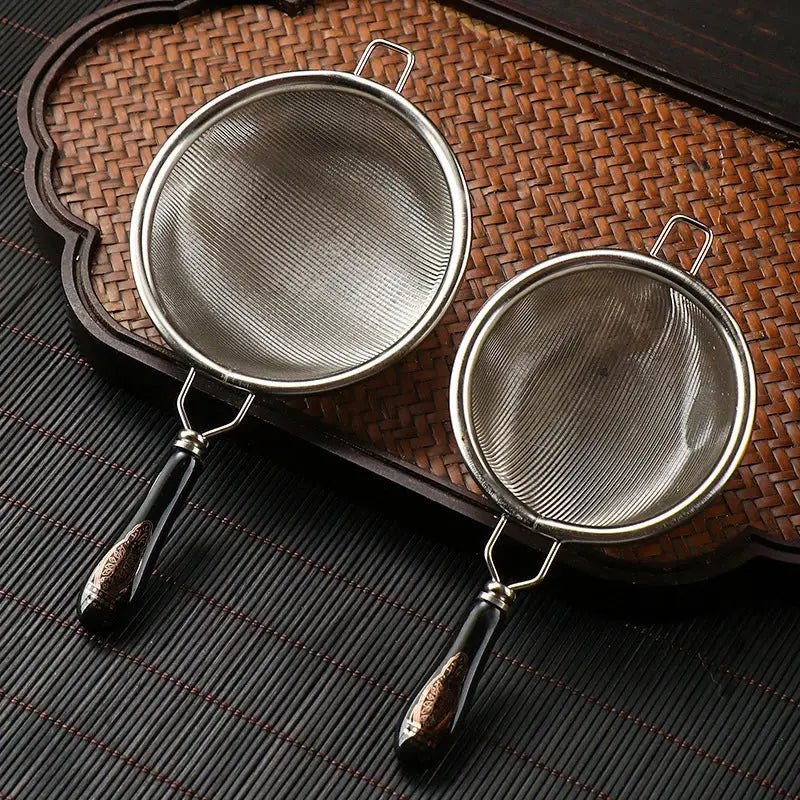 Stainless steel tea strainer resting on a ceramic cup rim