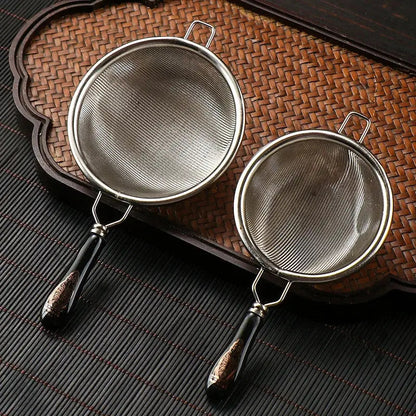 Stainless steel tea strainer resting on a ceramic cup rim