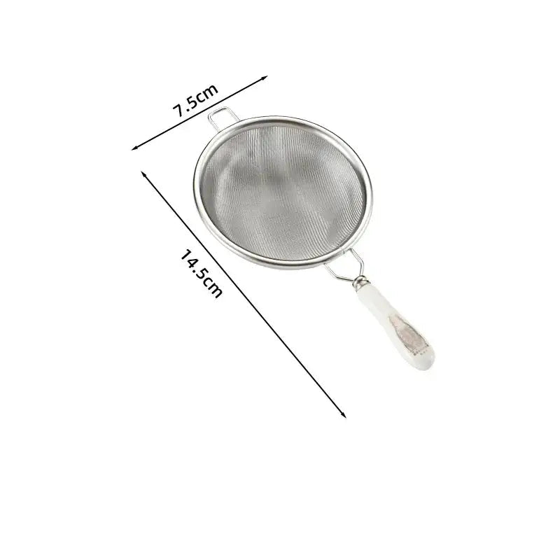 Silver tea strainer placed on a saucer next to a cast iron teapot