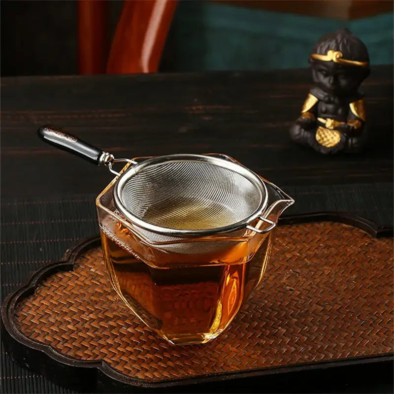 Hand holding stainless steel tea strainer over a cup of brewed tea